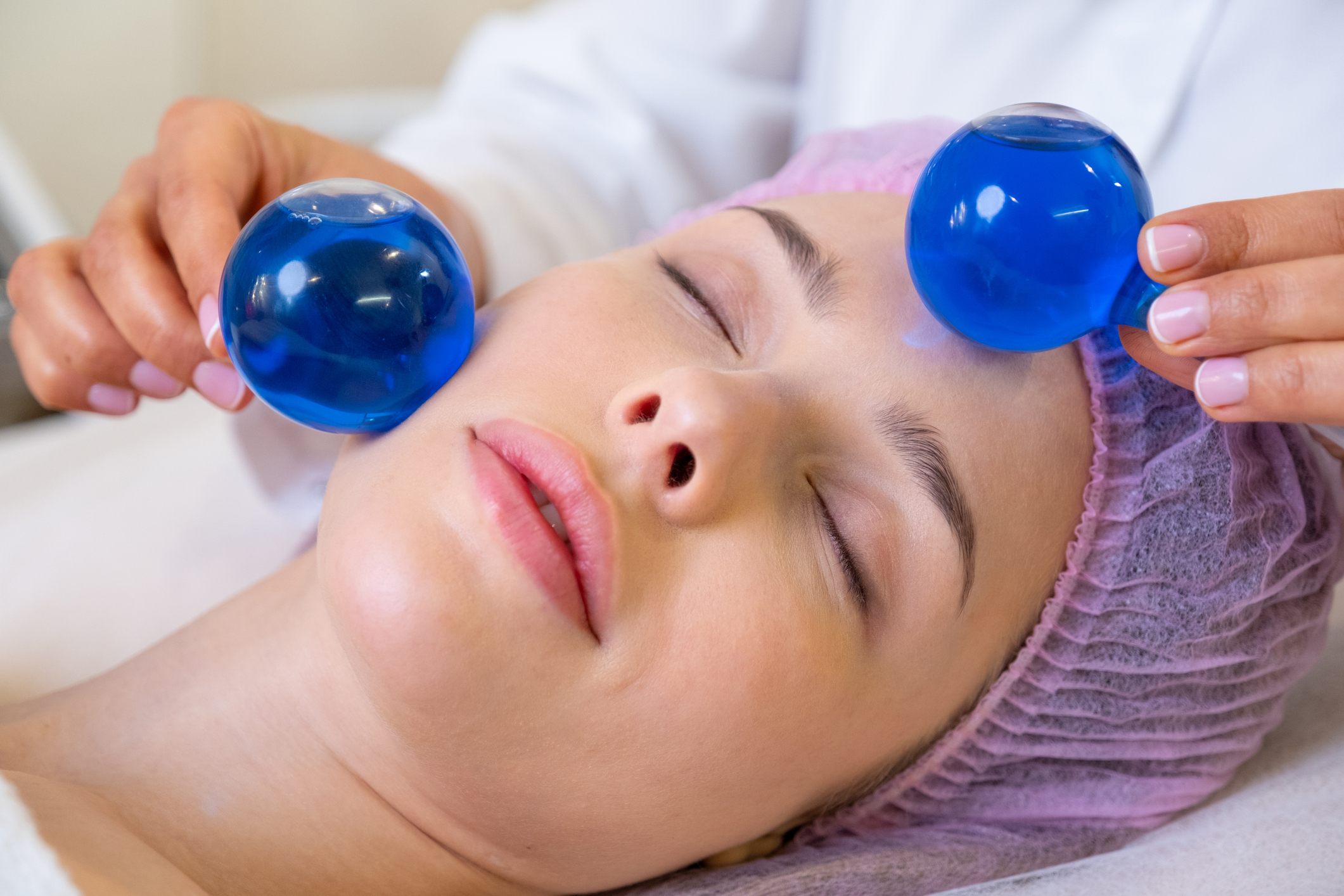 Beautician making a massage of the face using the blue balls. Woman in a spa salon on cosmetic procedures for facial care. Girl gets massage of a face. Cosmetologist makes face massage.